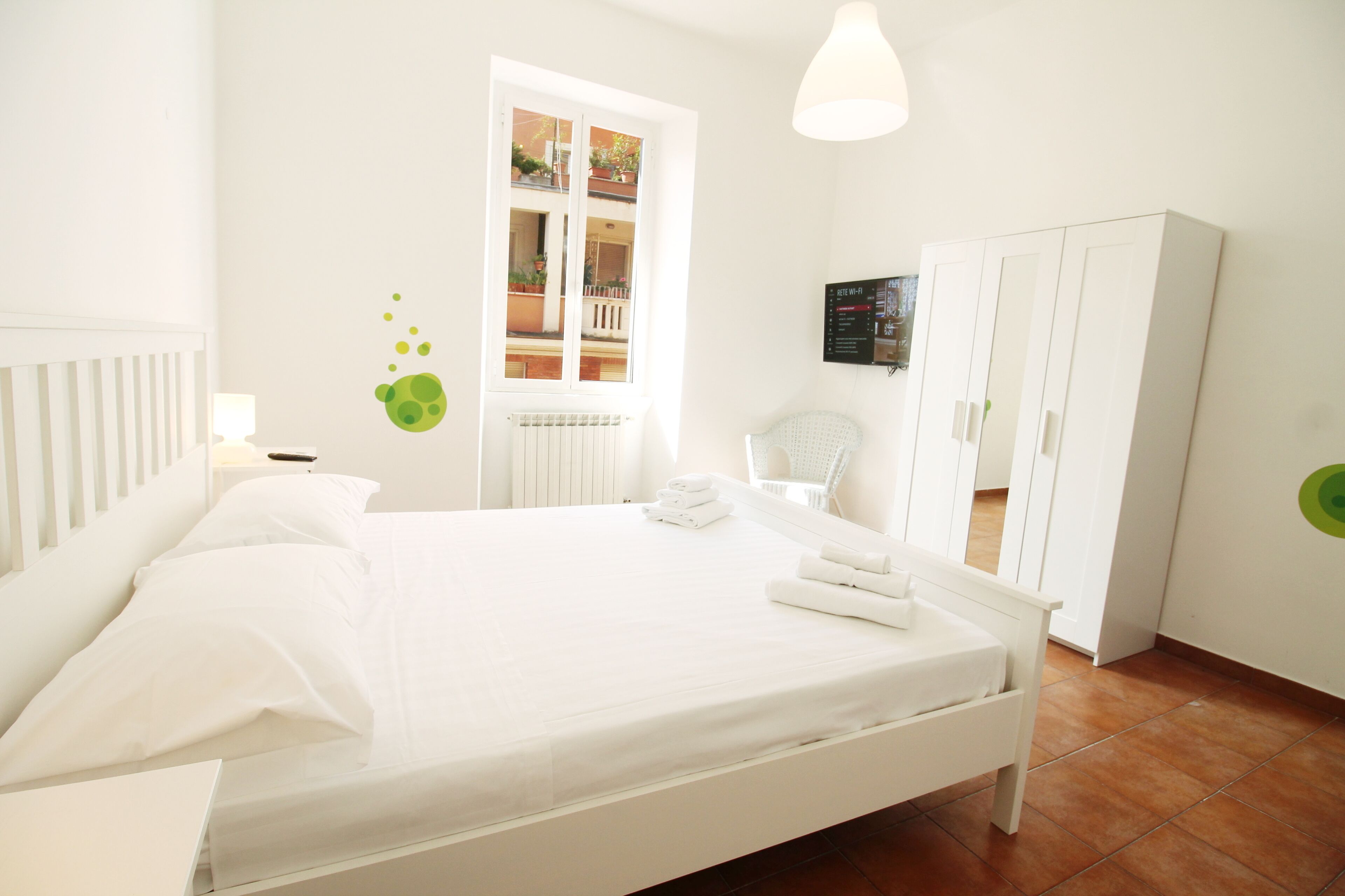 Een witte slaapkamer met een bed, een kledingkast, een raam en een bedieningspaneel aan de muur.