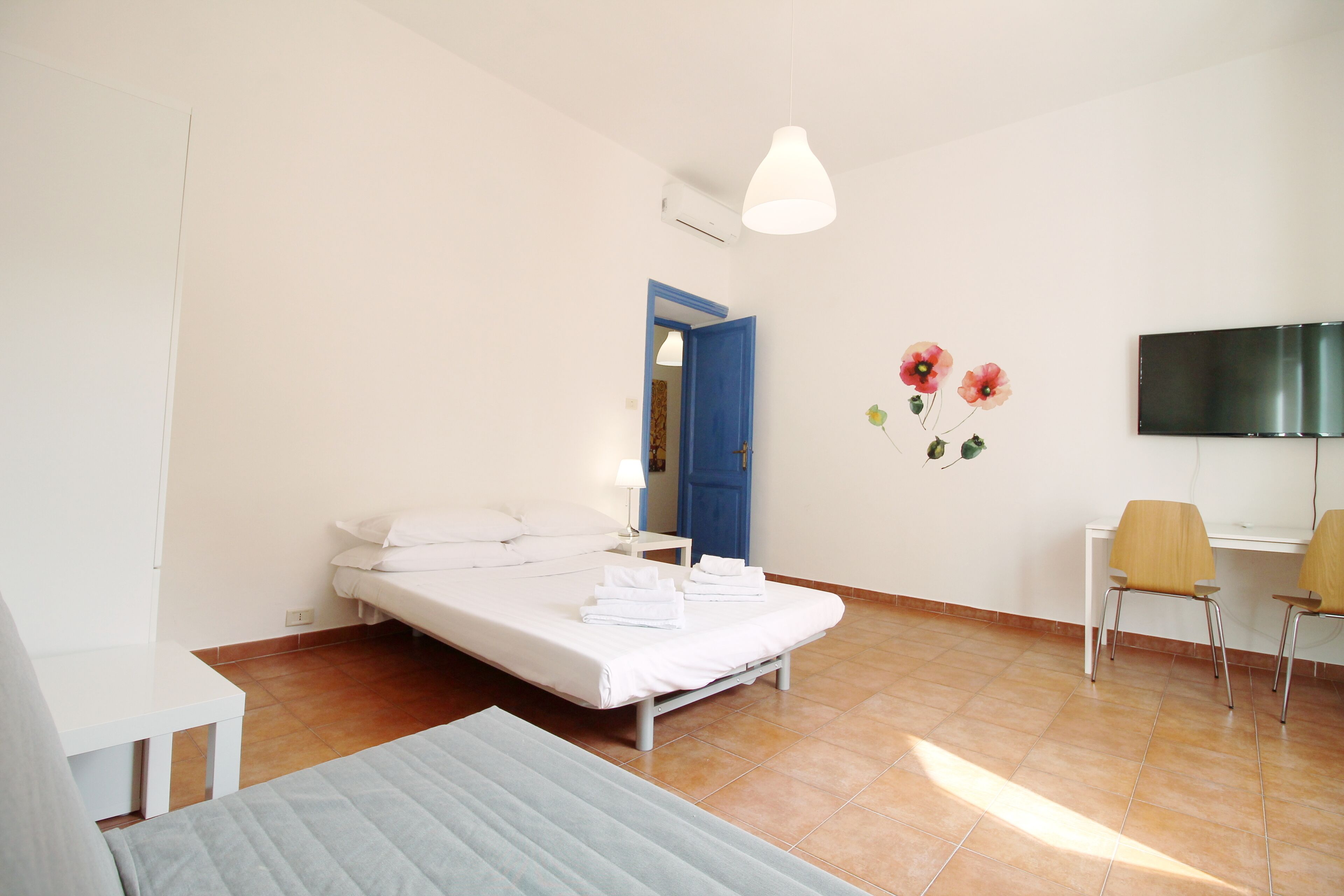 A bedroom with a bed, a desk, and a chair. There is a TV mounted on the wall.