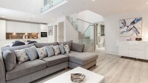 Una sala moderna con un sofá seccional gris, una mesa de centro blanca y una escalera que lleva a un nivel superior.