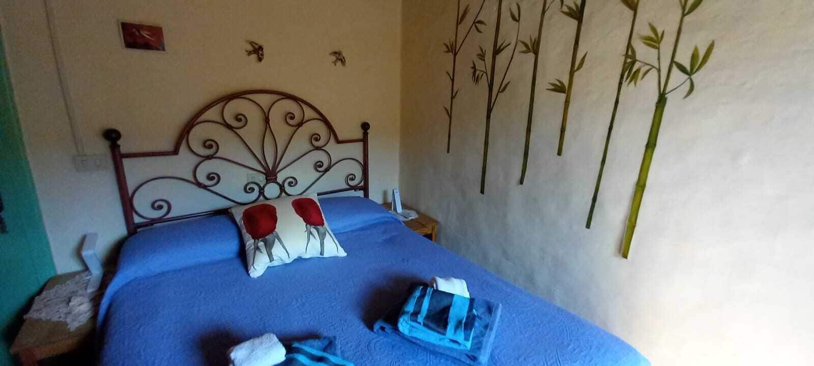 Ein Schlafzimmer mit einem Metall-Kopfteil, einer blauen Bettdecke, zwei roten Kissen und einem weißen Kissen, sowie einer Wand mit Bambus-Dekorationen.