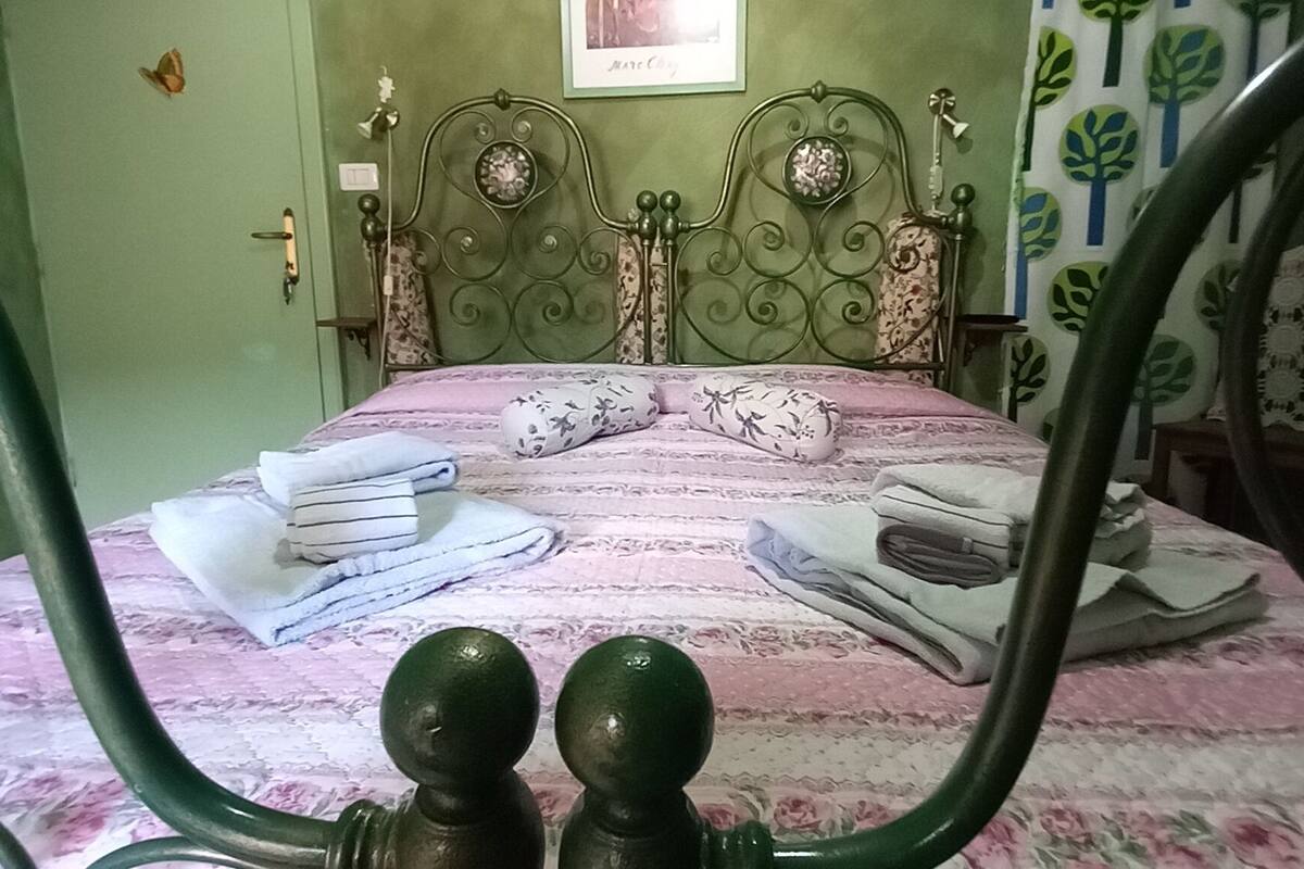 Uma cama com colcha florida, duas almofadas e toalhas dobradas.
