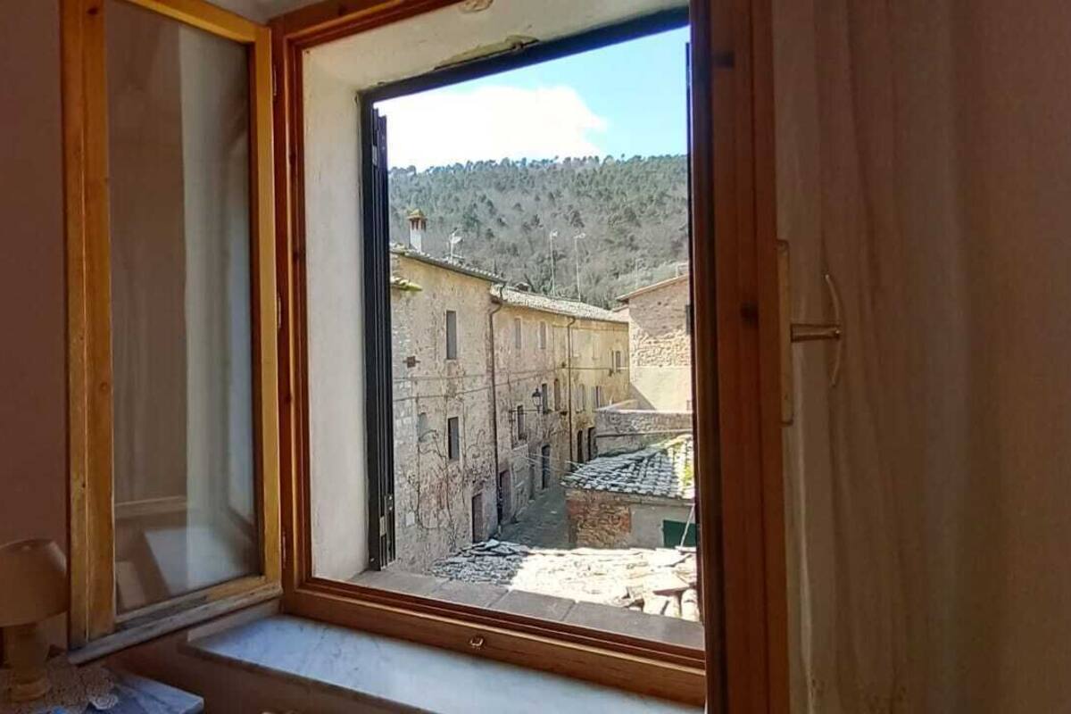Quarto com uma janela grande, uma cama, mesa de cabeceira e abajur.
