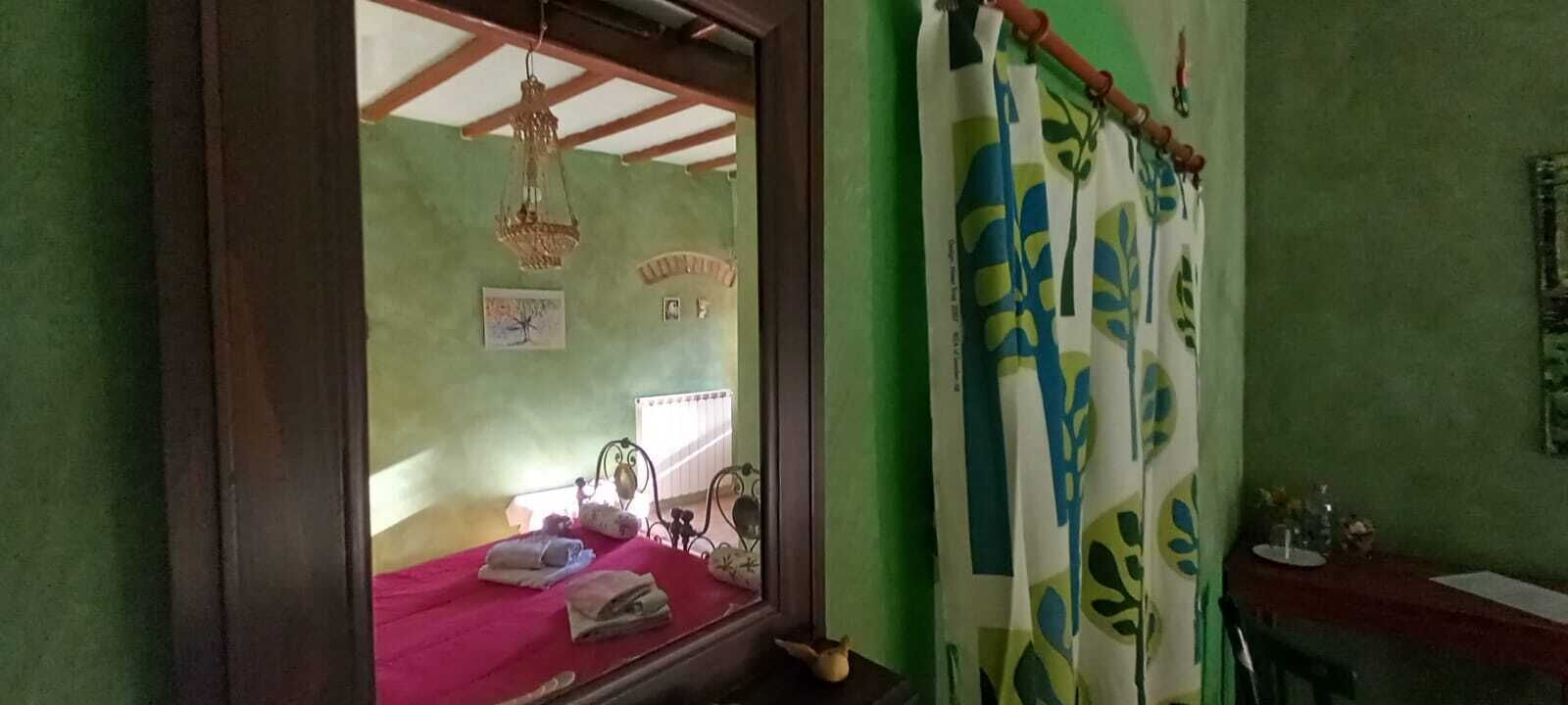 Un dormitori amb un llit, una finestra que dona a una altra habitació, una làmpada penjant i una cortina amb dibuixos de fulles.