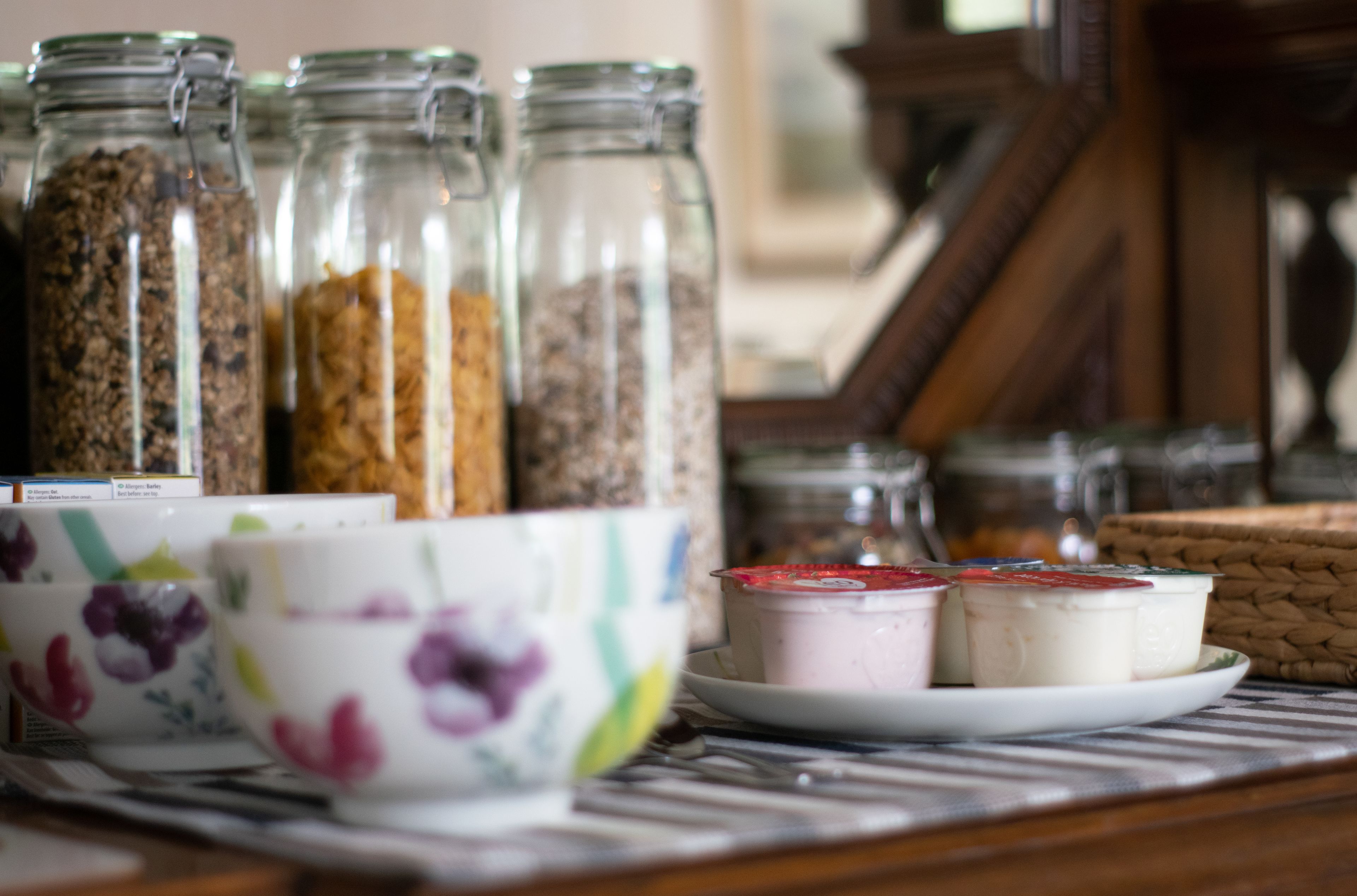 Una mesa con botes de granola y yogur, y tazas con estampado floral.