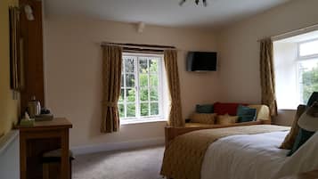 A bedroom with a bed, a window with curtains, a television on the wall, and a radiator.