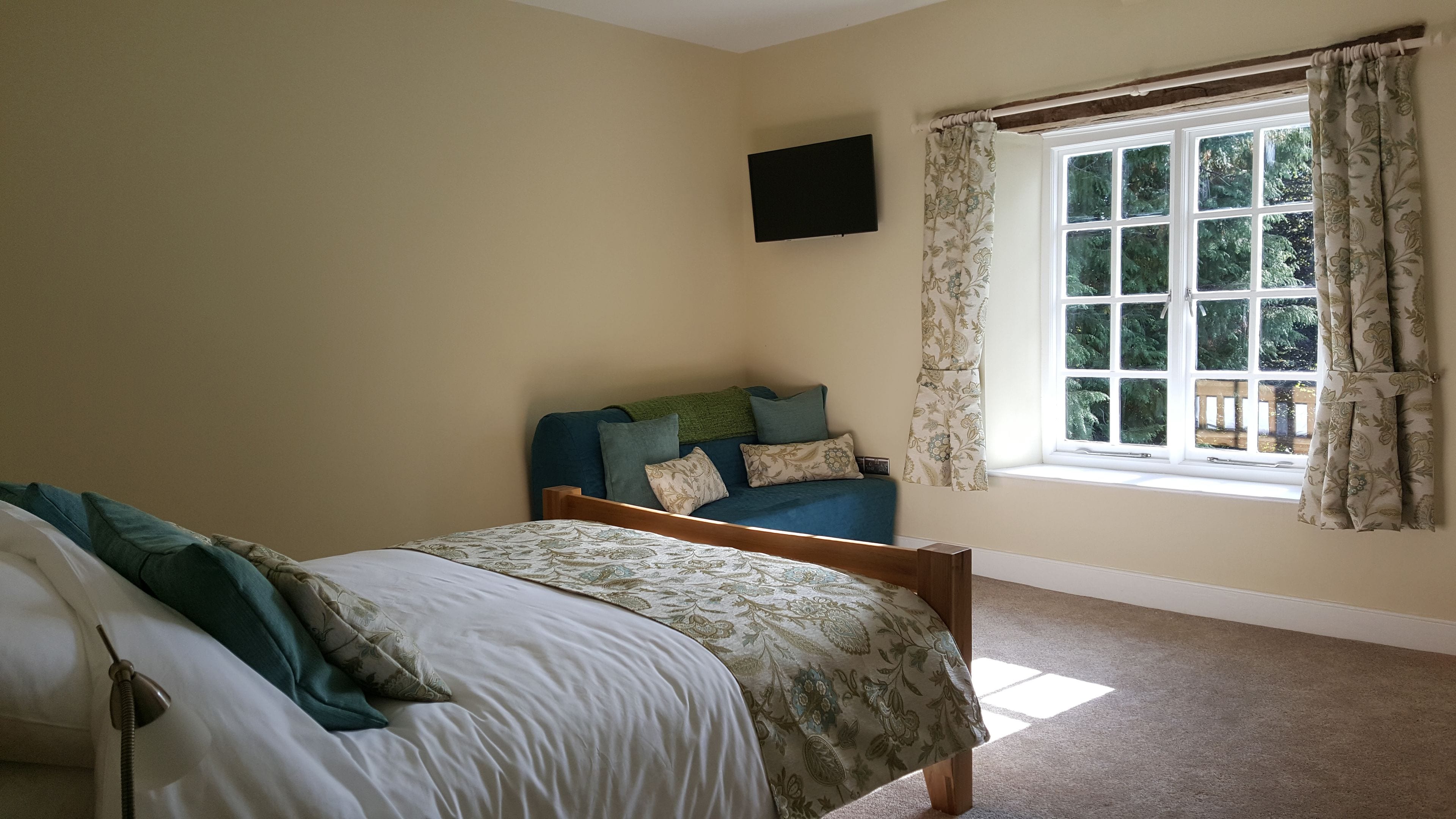 Um quarto com cama, sofá, televisão presa na parede e janela com cortinas.
