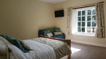 Une chambre à coucher avec un lit, un canapé, un téléviseur fixé au mur et une fenêtre avec des rideaux.