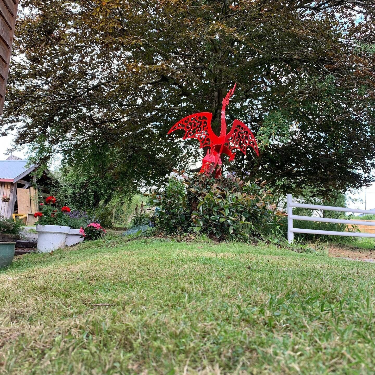 A red decorative sculpture in a garden area with a white fence and a wooden building in the background.
