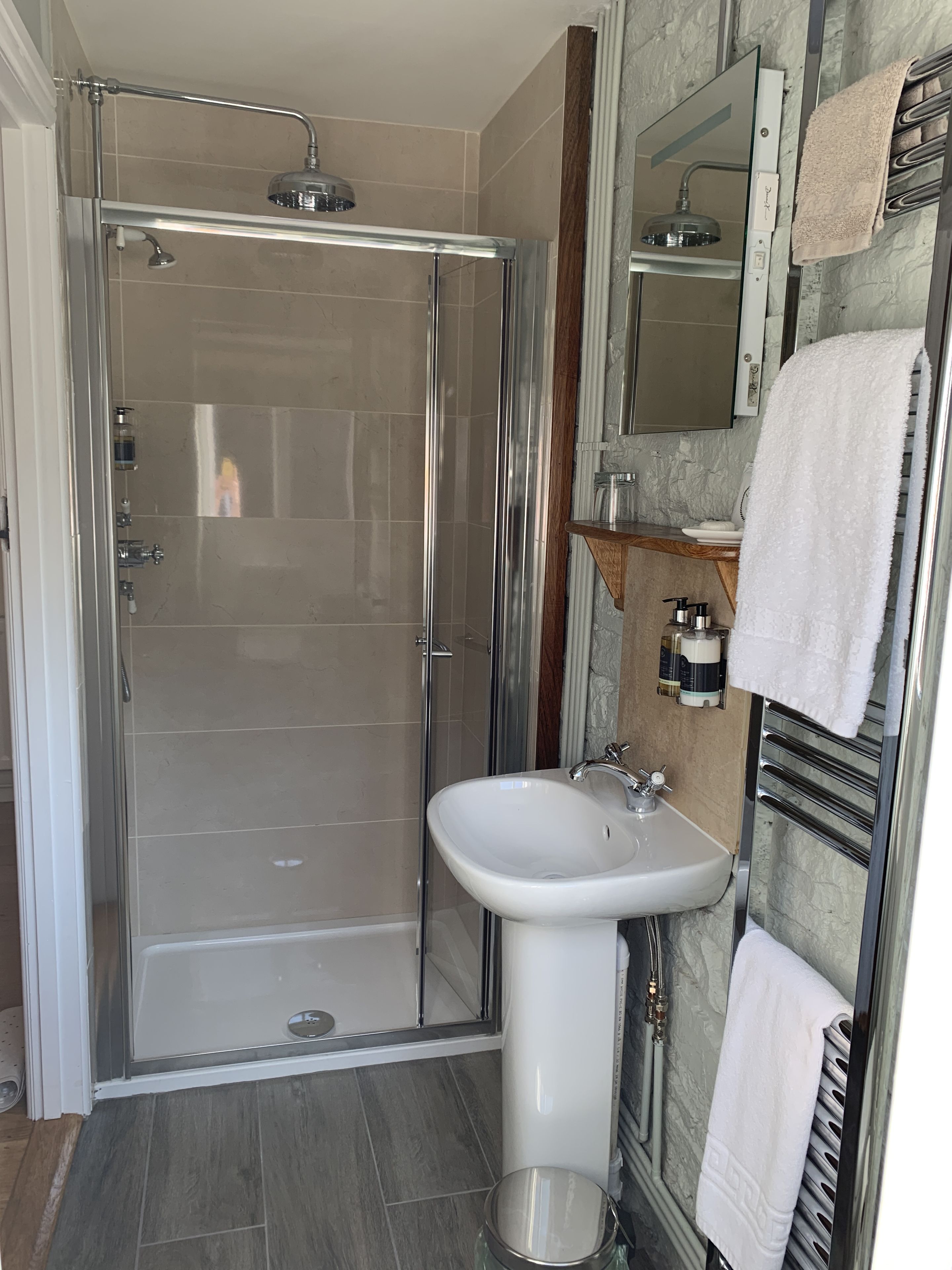 A modern bathroom with a glass-enclosed shower, a pedestal sink, and a vanity with a mirror.