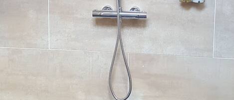 A shower with a handheld showerhead and a rain shower attachment, mounted on a wall with beige tiles.