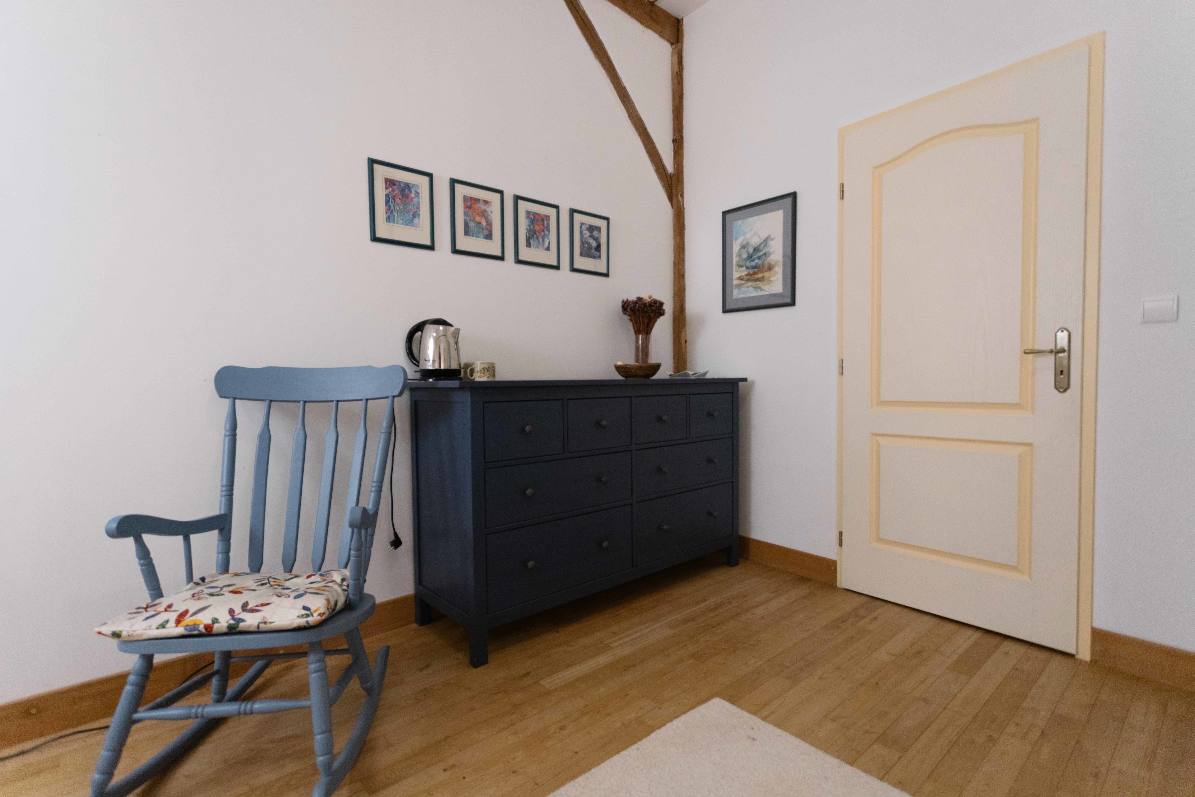 Una habitación con piso de madera, una mecedora azul, un aparador azul oscuro y una puerta blanca.