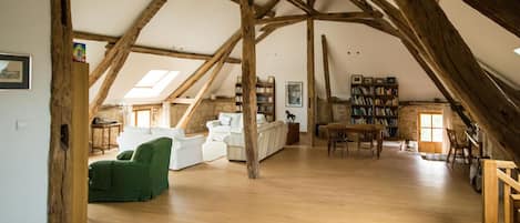 A spacious attic room with wooden beams, a white sofa, a green armchair, and a bookshelf.