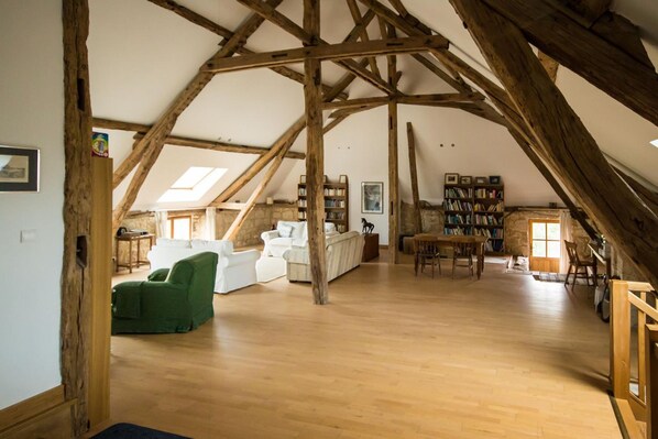A spacious attic room with wooden beams, a white sofa, a green armchair, and a bookshelf.