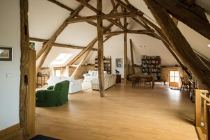 Um quarto espaçoso no sótão com vigas de madeira, um sofá branco, uma poltrona verde e uma estante de livros.