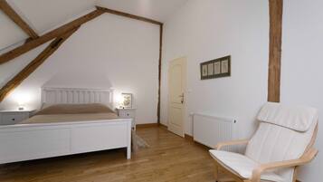 Une chambre avec un plafond en pente, un lit, une table de chevet, une chaise et une porte.