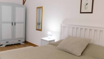 A bedroom with a bed, a nightstand, a wardrobe, a mirror, and a framed picture on the wall.