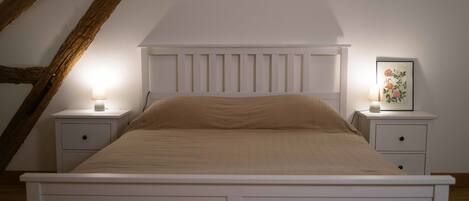Ein Schlafzimmer mit einem weißen Bett, zwei Nachttischen mit Lampen und einem gerahmten Bild auf einem Tisch.