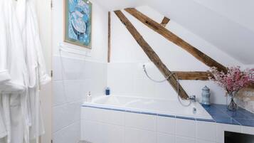 Un bagno con una vasca, piastrelle bianche, travi in legno, un porta asciugamani e un quadro appeso al muro.