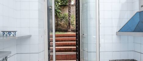 Una cocina moderna con baldosas blancas, encimeras de granito, horno empotrado y puerta de cristal que da a una escalera.
