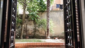 A view through a metal gate into a courtyard with brick steps leading to a building entrance. - Lush Garden Steps Away from Great Park (Rome)