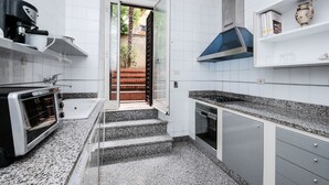 A modern kitchen with a built-in oven, a coffee maker, and a range hood. There is a set of stairs leading to a patio area. - Lush Garden Steps Away from Great Park (Rome)