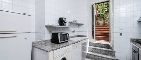 Uma cozinha compacta com armários brancos, máquina de lavar embutida, micro-ondas e cafeteira.