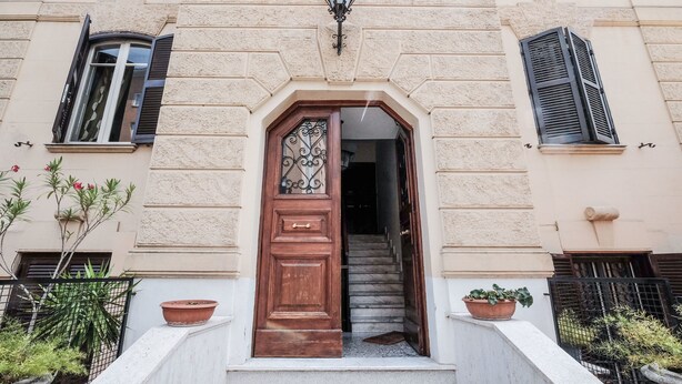 A building entrance with a wooden door, a staircase leading inside, and potted plants on the steps. - Lush Garden Steps Away from Great Park (Rome)