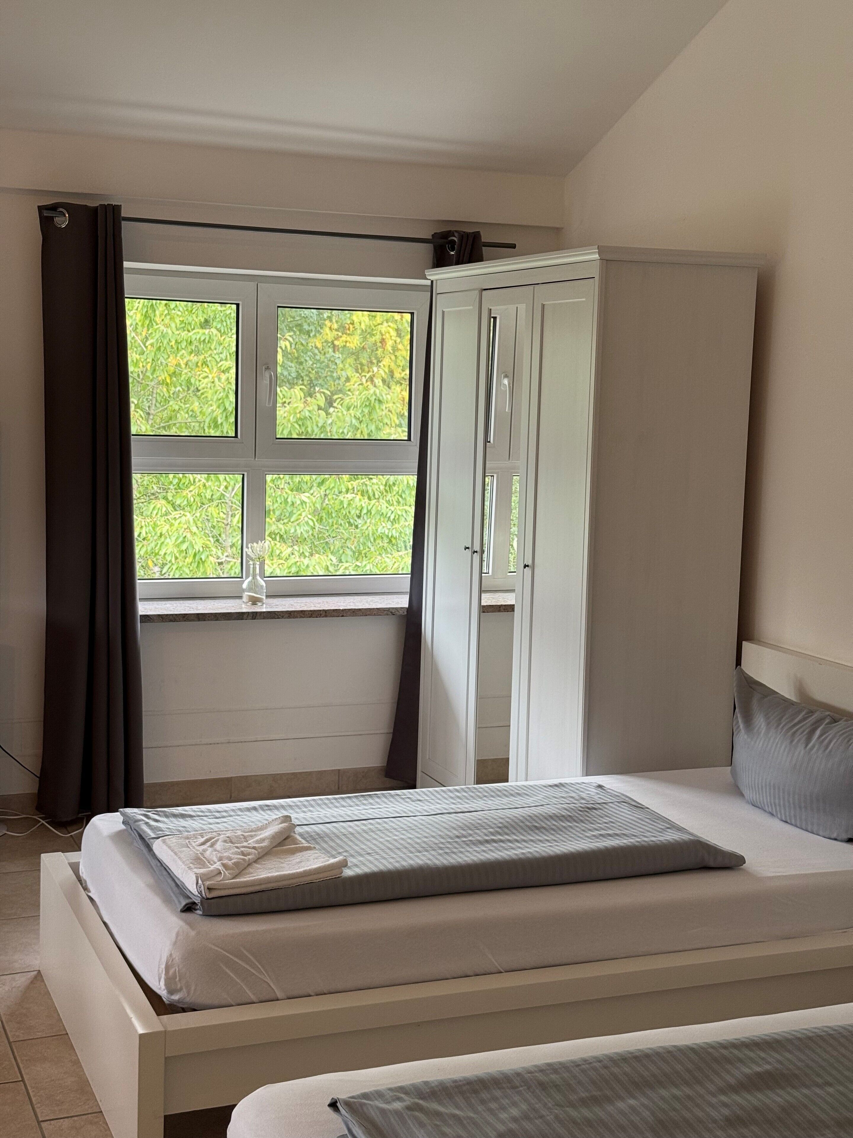 A bedroom with a bed, a wardrobe, and a window with curtains.