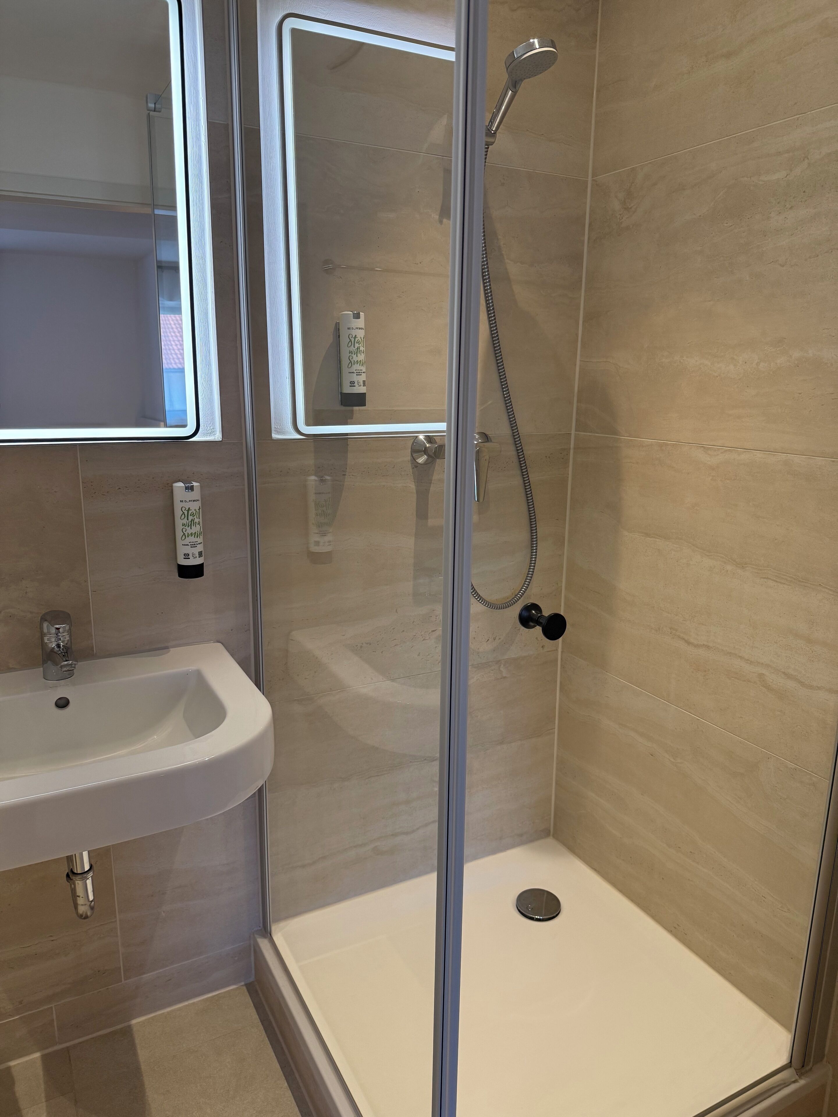 Un baño moderno con ducha de vidrio, lavamanos blanco y espejo.