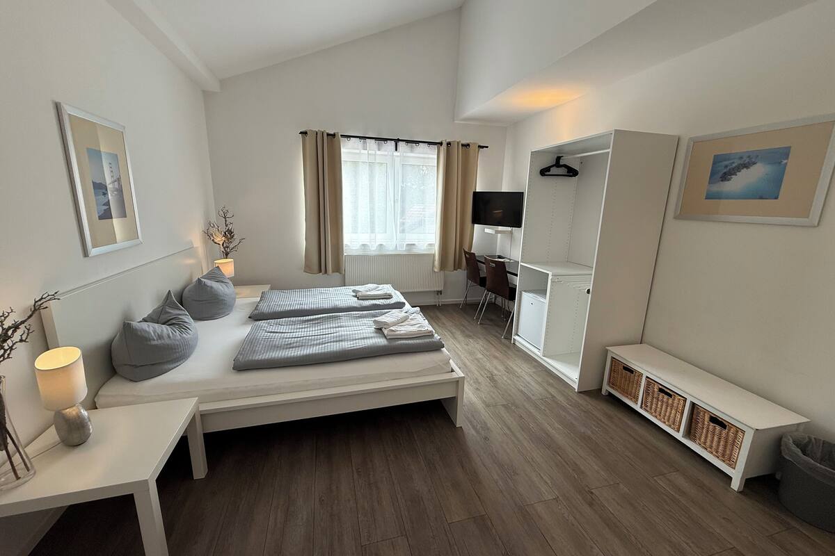 A modern, well-lit bedroom with a bed, bedside tables, a desk, and a TV.