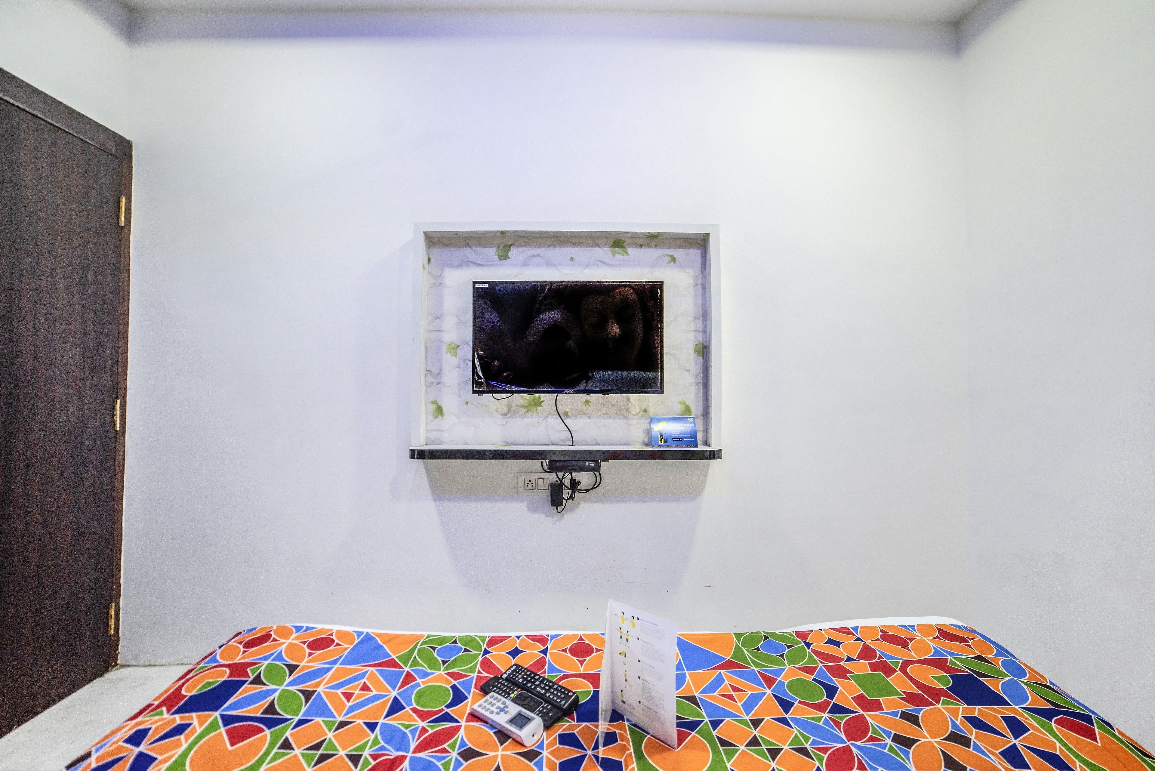A room with a bed, a small TV mounted on the wall, and a calendar on the bed.