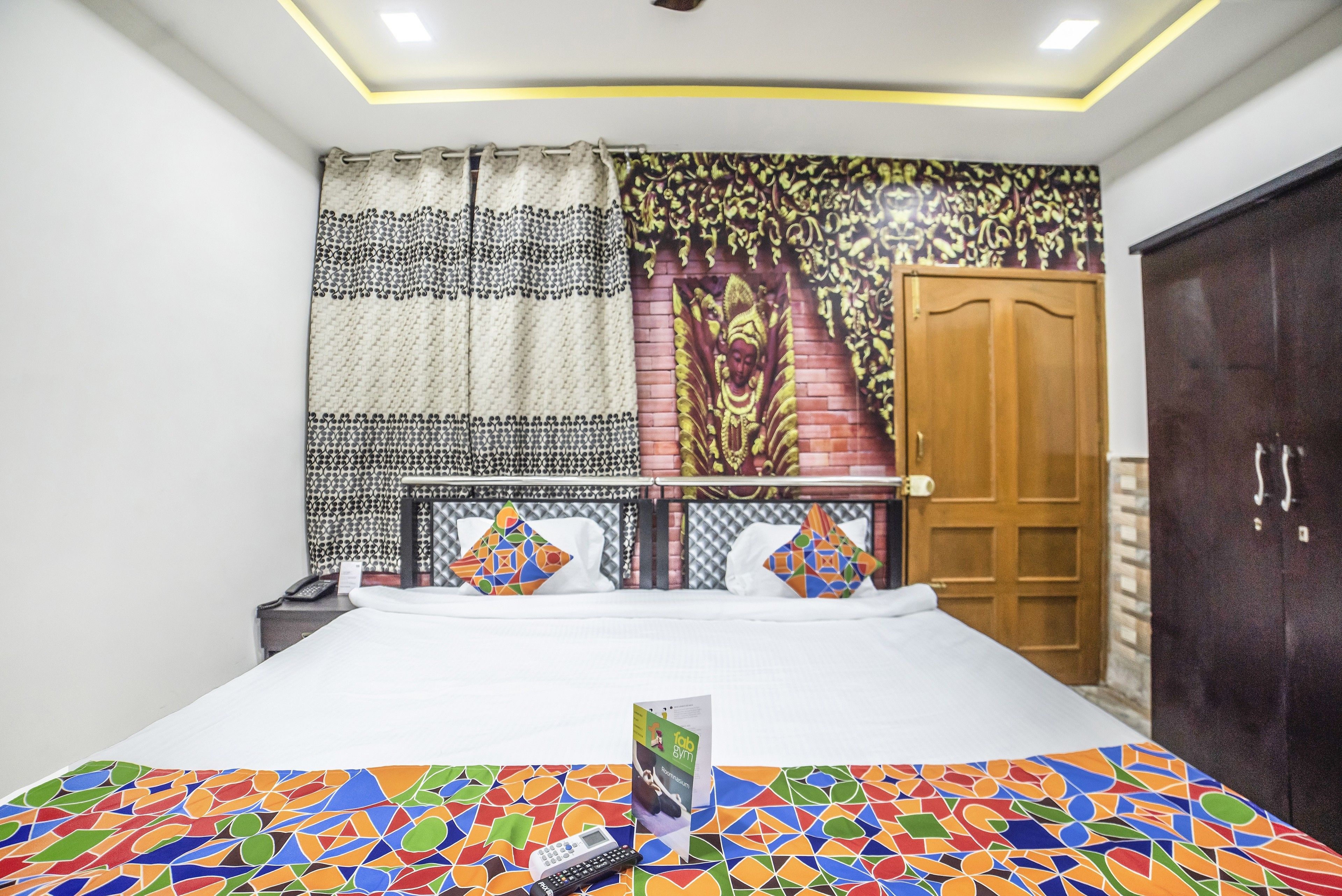 A hotel room with a bed, a nightstand, a telephone, a brochure, a tapestry, and a wardrobe.