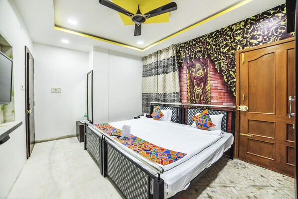 A bedroom with a bed, a ceiling fan, a patterned wall, and a wooden door. - FabHotel ABC View (Indore)