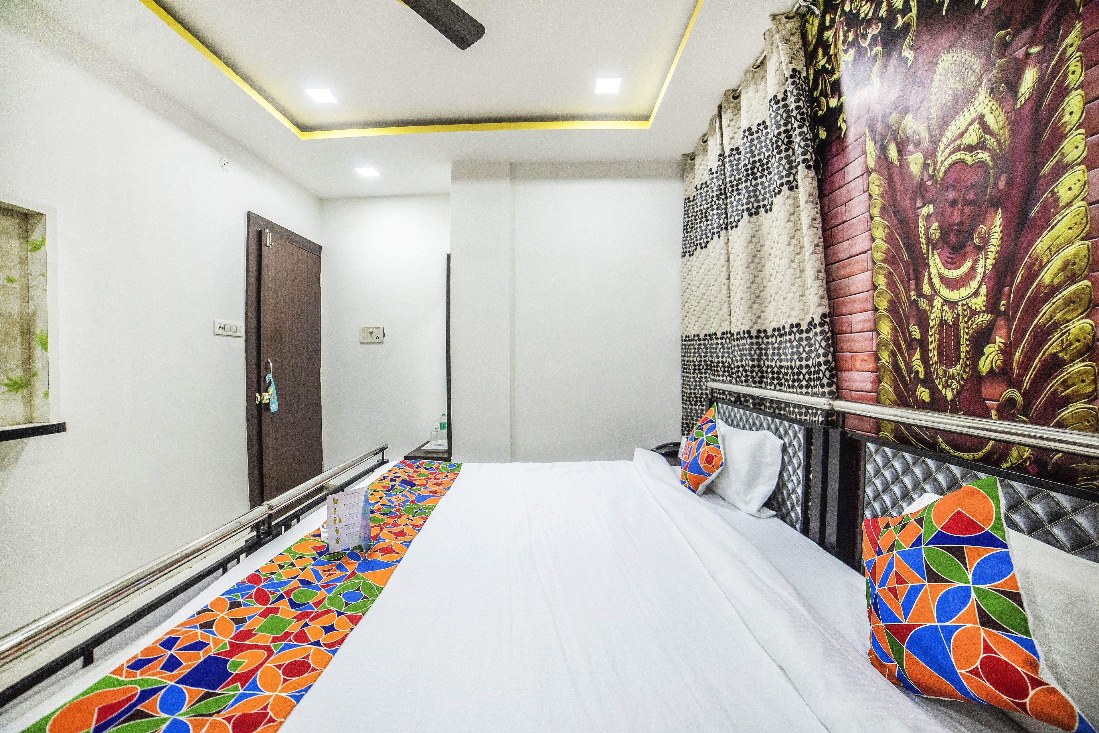 A hotel room with a bed, a headboard with a mural, a patterned runner, and a door.