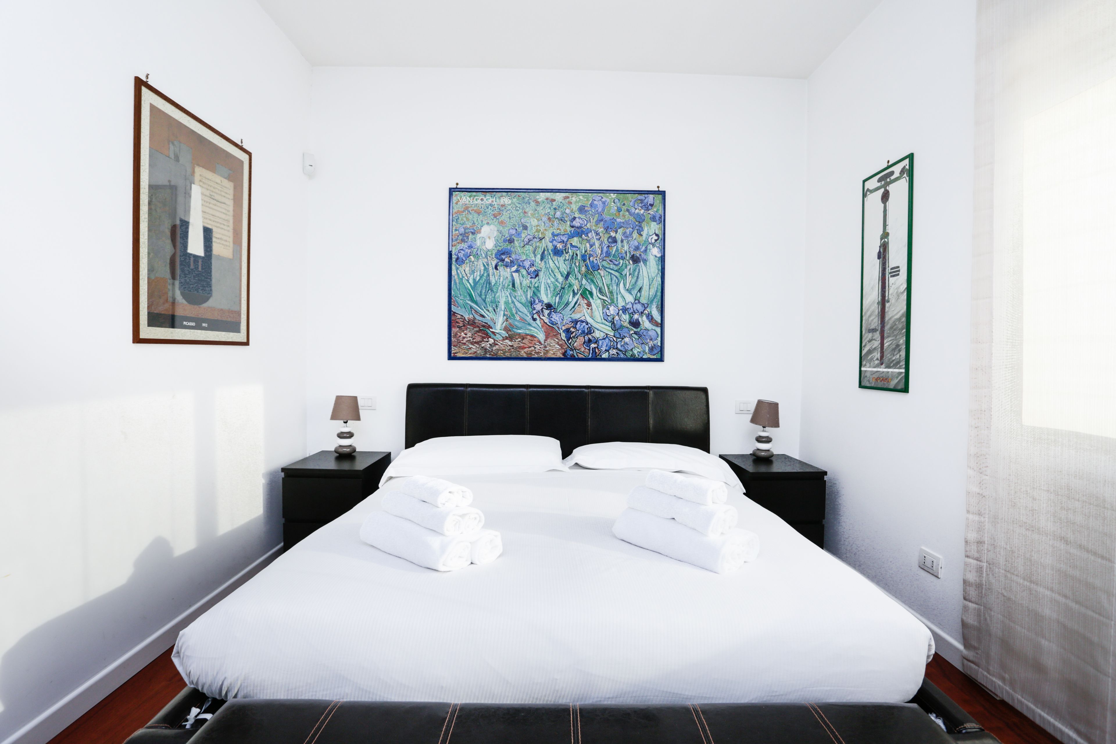 Una habitación de hotel con una cama grande, dos mesitas de noche con lámparas y tres cuadros enmarcados en las paredes.