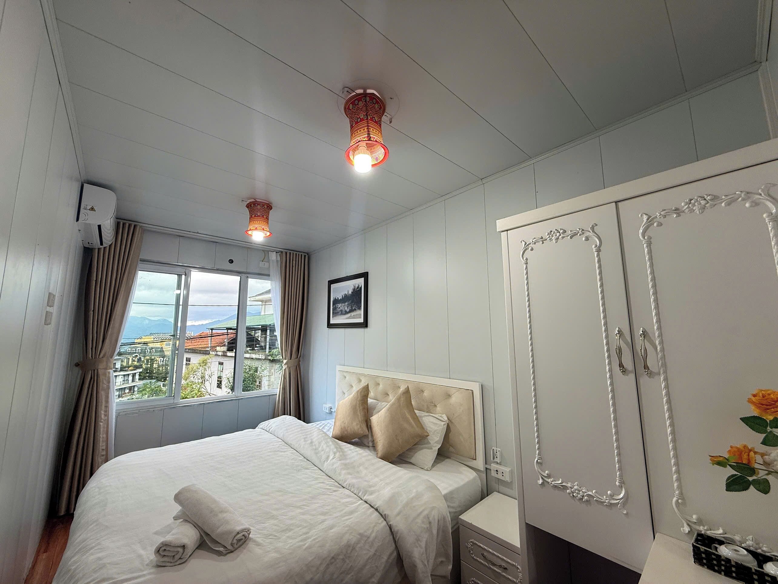 A bedroom with a bed, a wardrobe, a window with curtains, and a picture on the wall.