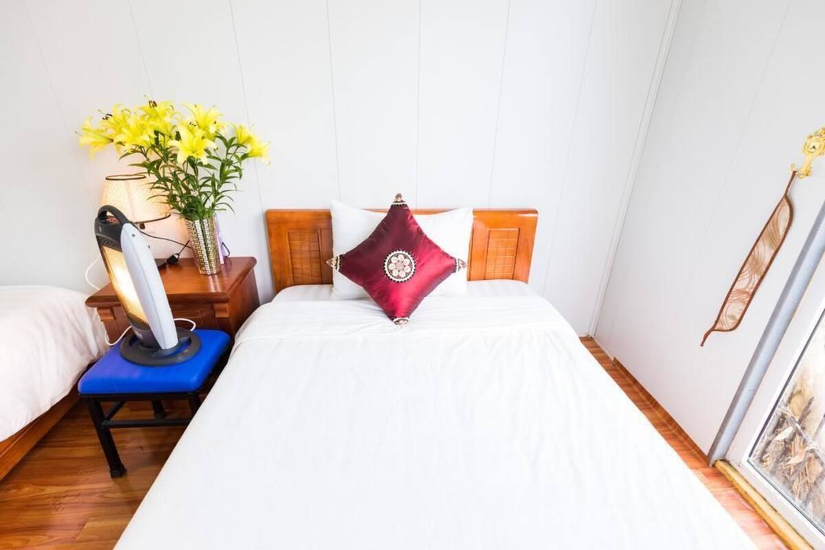 A hotel room with a bed, a nightstand with a lamp, a vase with flowers, and a window with a view of the outside.