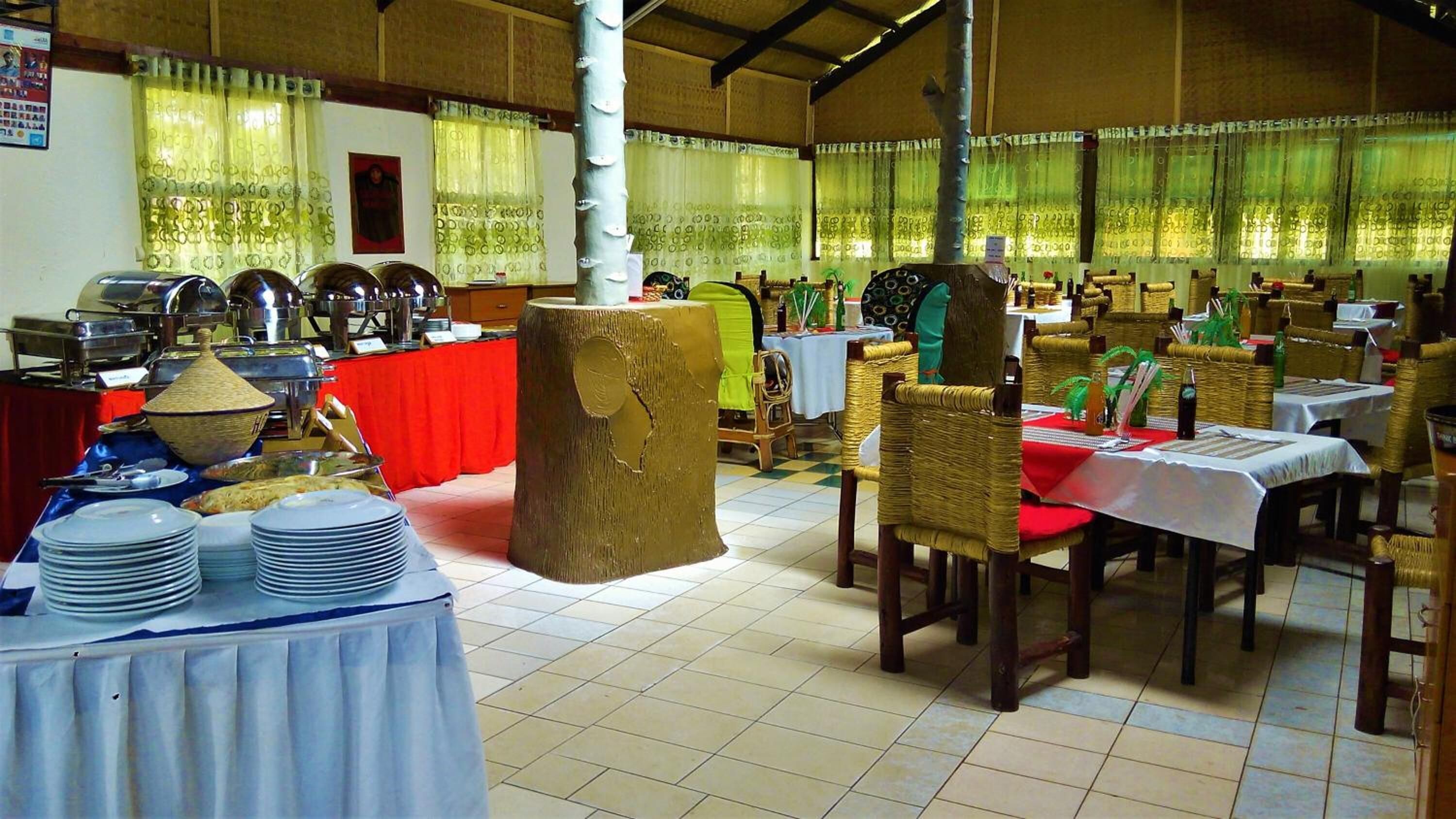 Un comedor con mesas dispuestas para comidas, un bufé con diversos platos y un gran tronco de árbol decorativo.