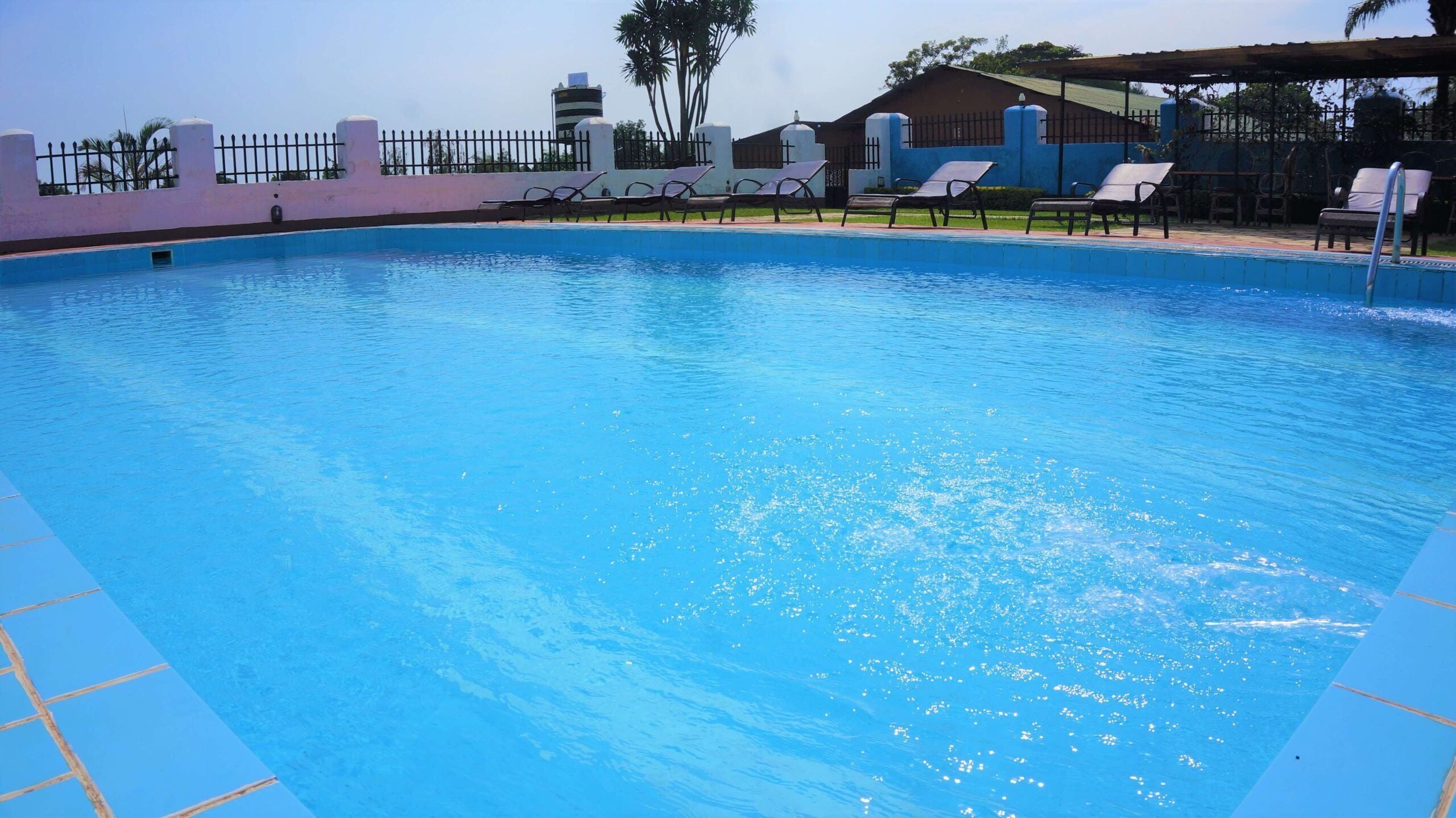 A swimming pool with clear blue water, surrounded by lounge chairs and a fence.