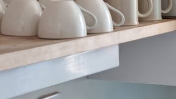 Una cocina con estantes de madera que sostienen tazas y platos de cerámica blanca.