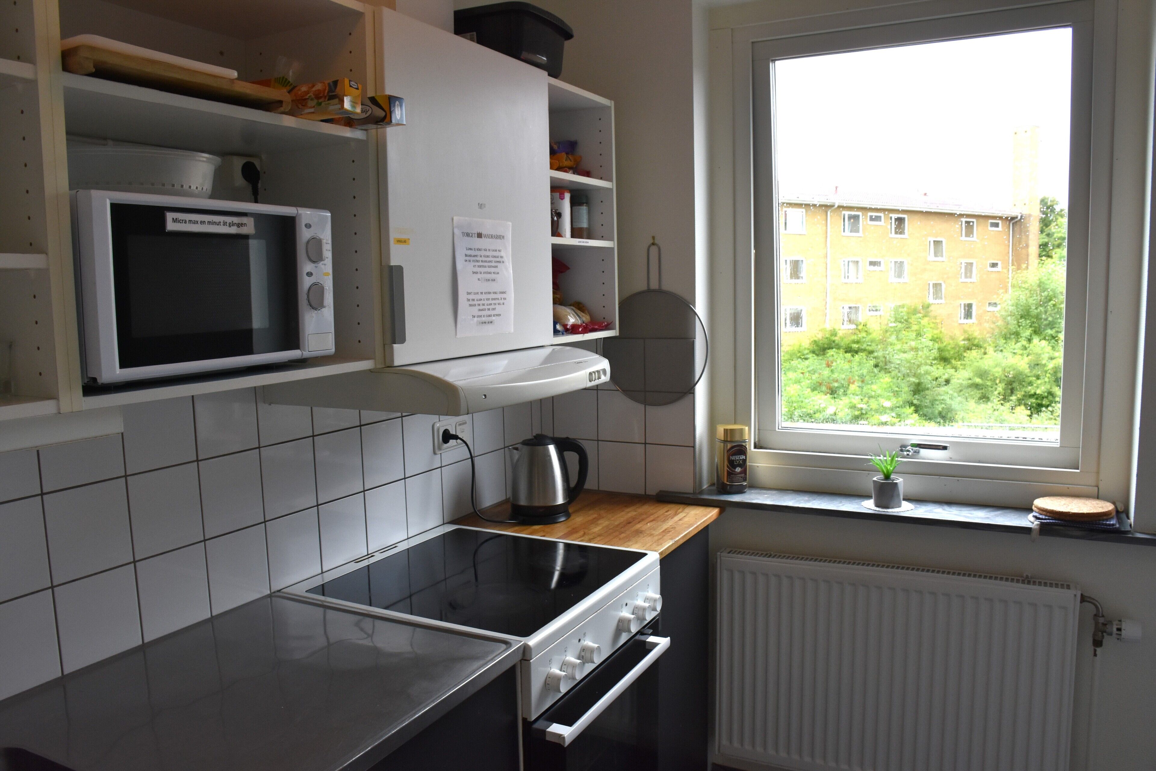 Una cocina con microondas, estufa y ventana que ofrece vistas a edificios y zonas verdes.