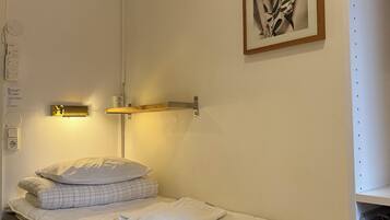 Una cama individual con colchón acolchado, una mesita de noche con lámpara, y un cuadro en la pared.