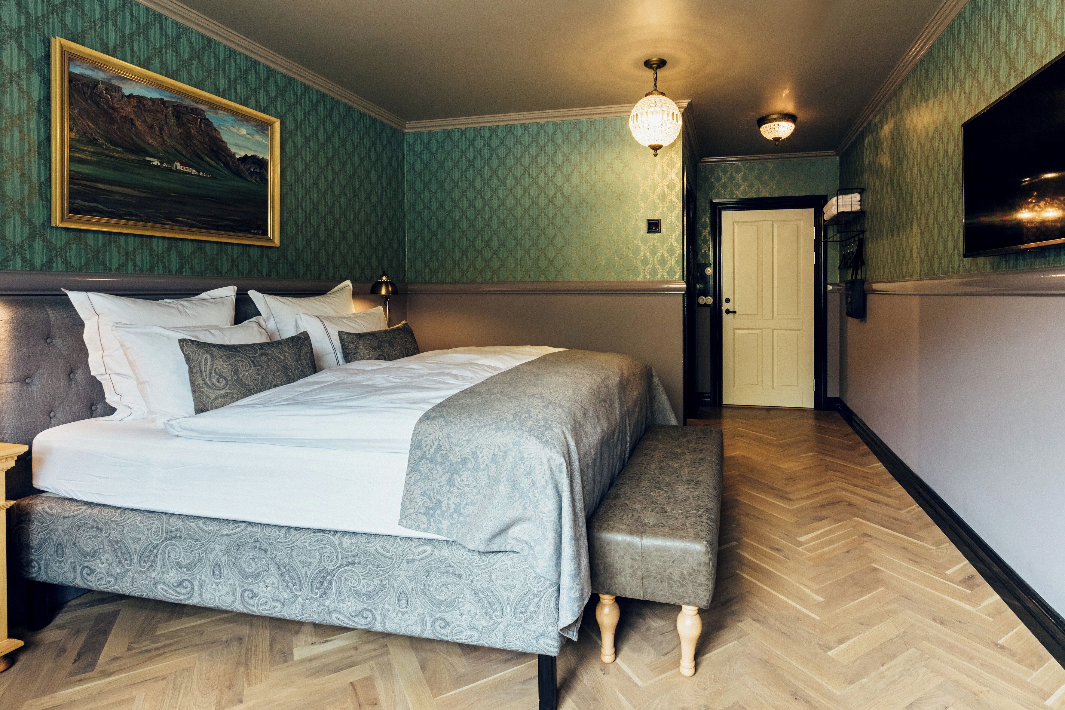 A bedroom with a bed, bench, and a painting on the wall.