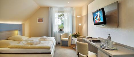 A hotel room with a bed, a desk, a chair, a TV, and a window with curtains.
