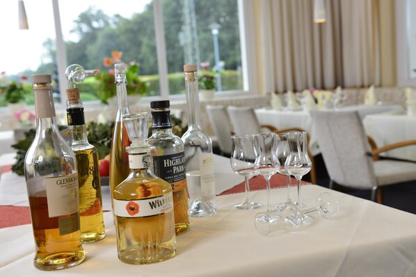 A table with various bottles of alcohol and wine glasses, set in a well-lit room with a view of greenery outside. - AKZENT Hotel Haus Surendorff (Bramsche)