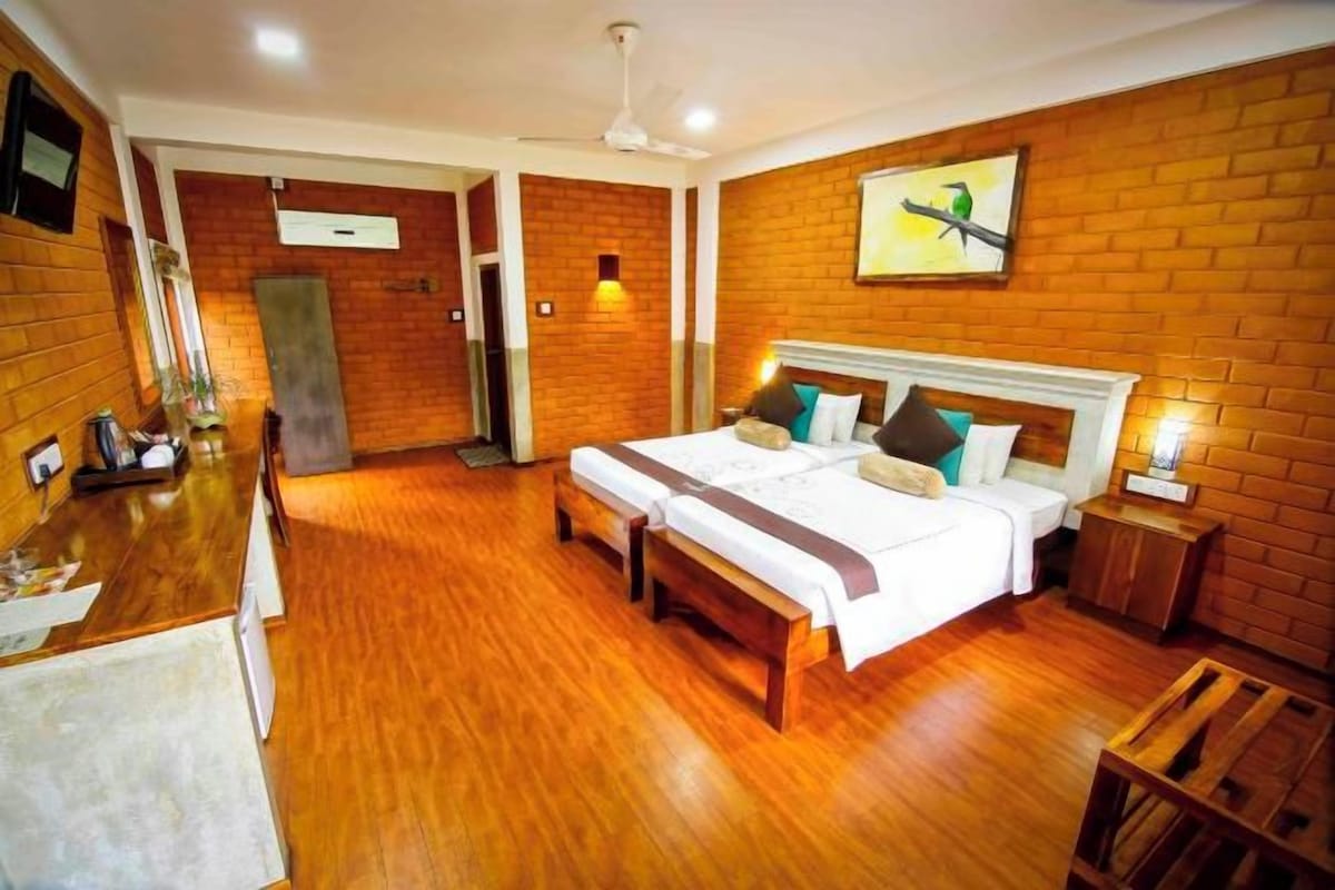 A hotel room with a brick wall, a bed with two pillows, a bedside table, and a wooden floor.