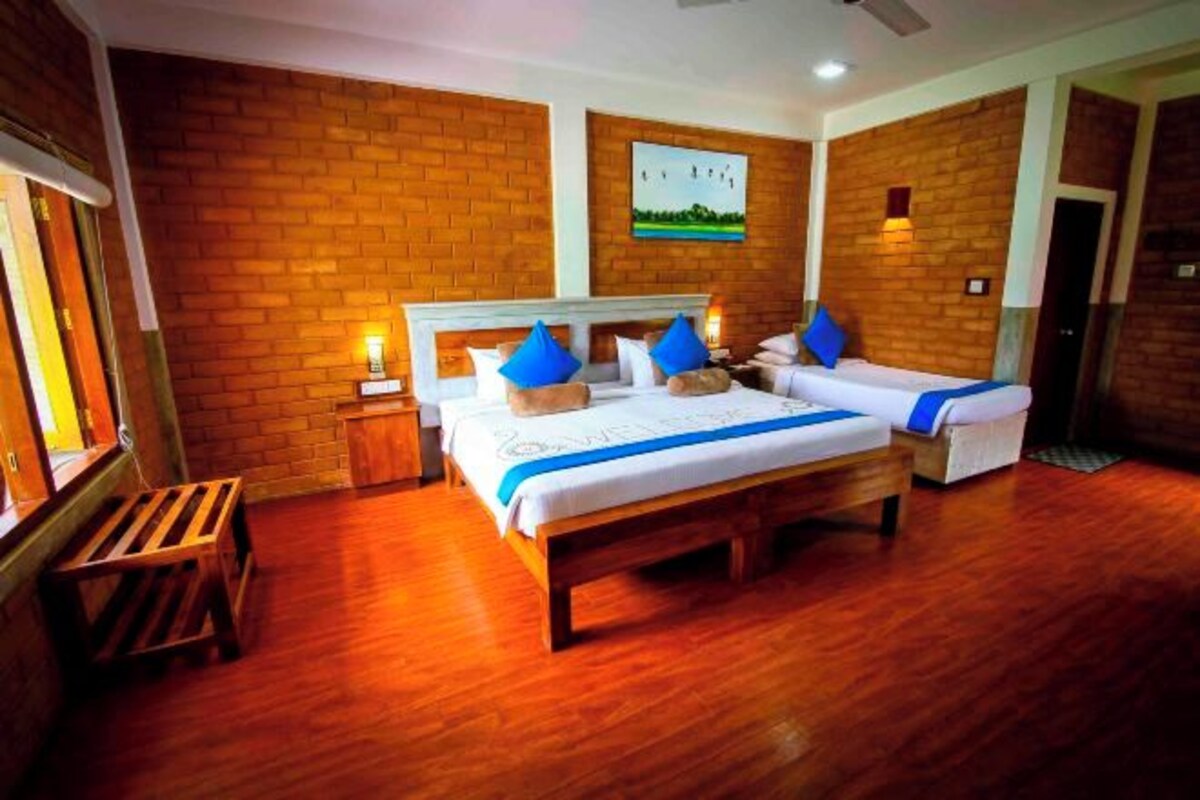 A hotel room with two beds, wooden flooring, a brick wall, and a painting.