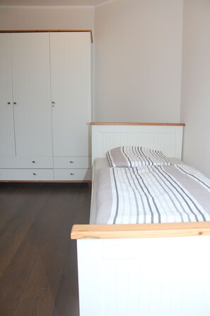 A bedroom with a bed, a wooden headboard, a wardrobe, and a wooden floor.