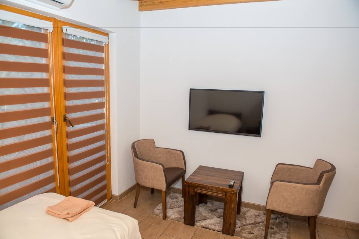 A bedroom with a bed, a TV mounted on the wall, and two chairs.