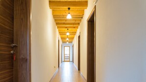 Un couloir avec des poutres en bois au plafond, un sol carrelé et une porte sur le côté gauche.